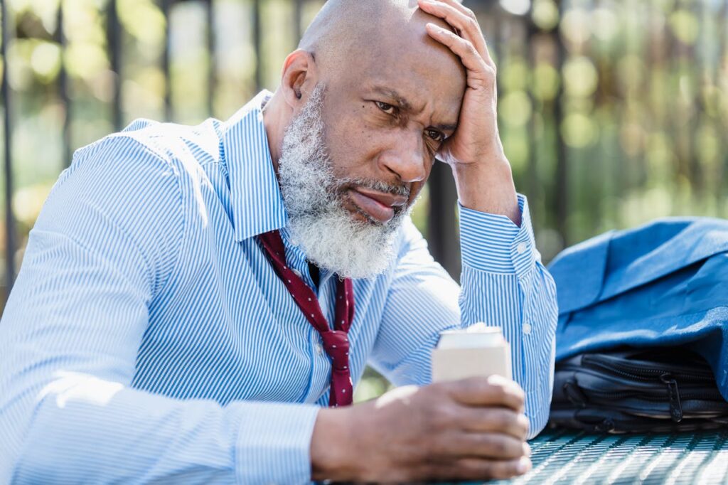 Sad black businessman with alcohol drink on street